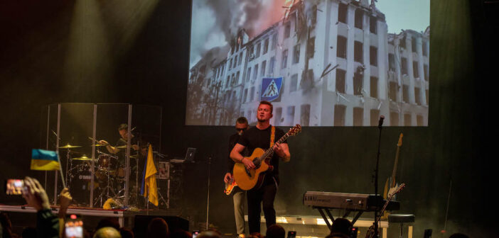 Igor Rybar performing in front of an image of a burning building during the war