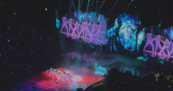 Image of a stage at a k-pop concert with the group members dancing on stage