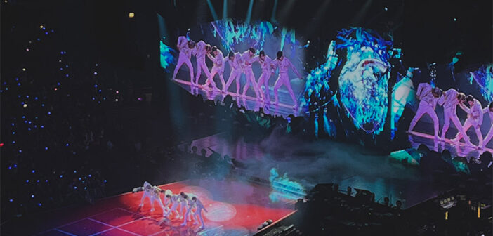 Image of a stage at a k-pop concert with the group members dancing on stage